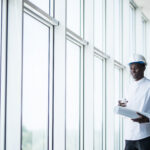 Afro american construction engineer in front of building holding blueprints